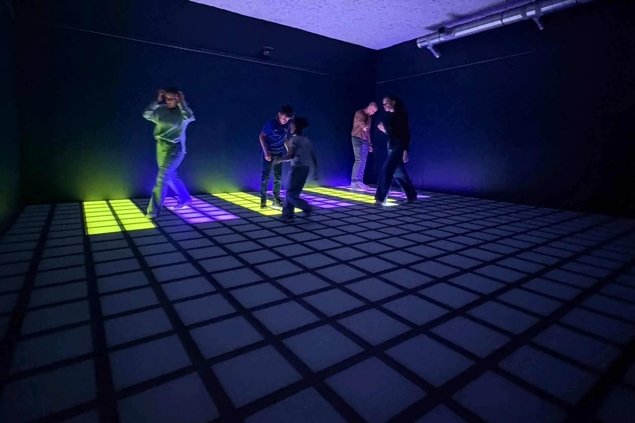 Joueurs en pleine partie dans la salle PIXEL ROOM, dalles lumineuses au sol