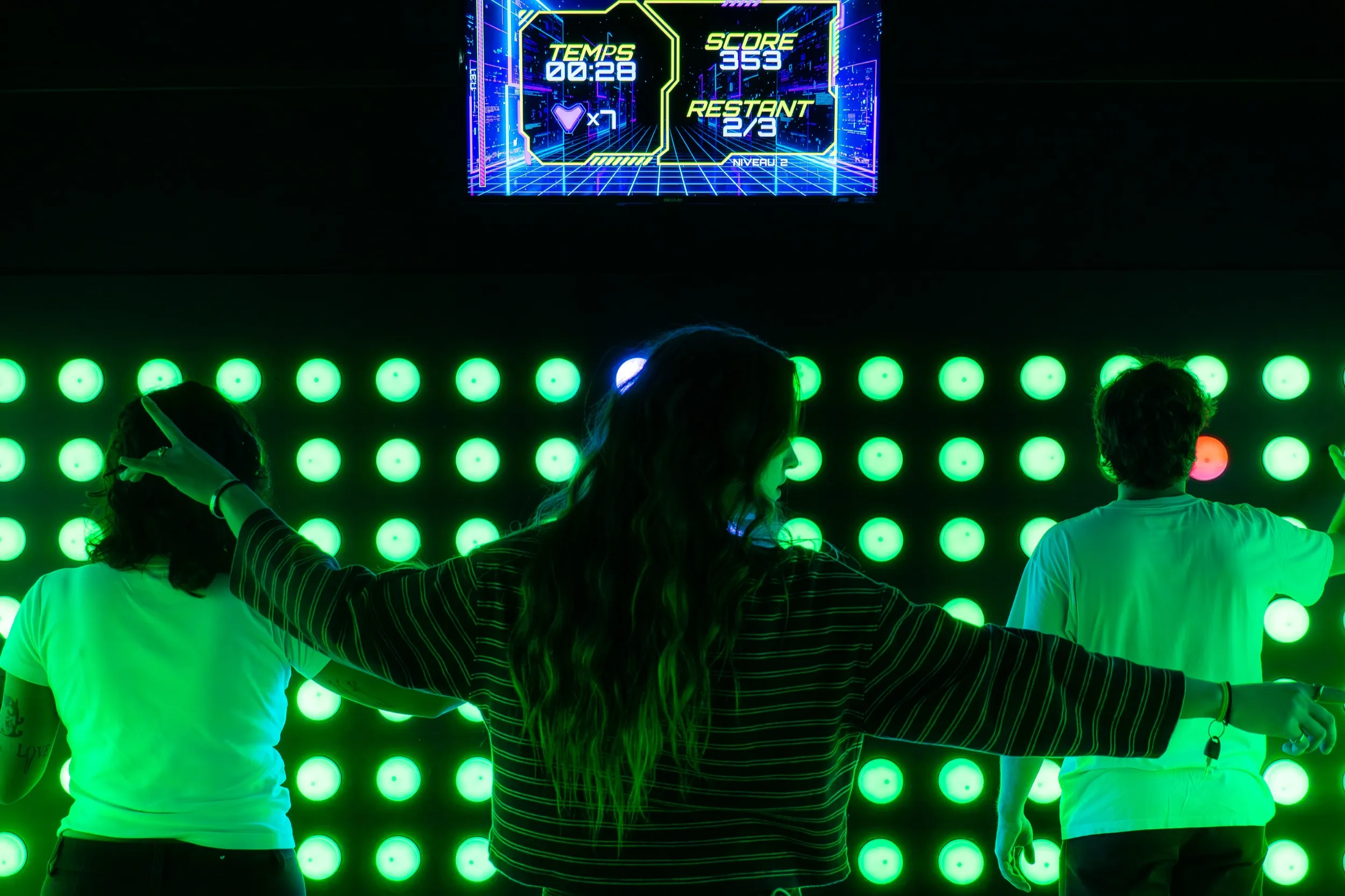 Joueurs face au mur PUSH ARENA illuminé en vert, score affiché à l'écran
